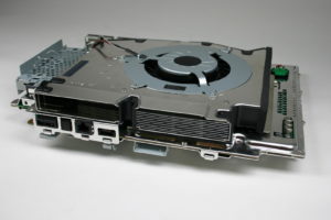 Abbildung 1: Massive Kühlung: Der Lüfter der PS3 hat einen Durchmesser von rund 15 Zentimetern und wiegt 500 Gramm. Der Kühlkörper bringt nochmal so viel auf die Waage. Darunter befindet sich zwischen zwei Metallplatten das rund 30 x 25 Zentimeter große Mainboard.