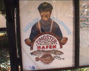 Abbildung 1: Besser als jeder Titel: Das Schild weist den Zuschauer darauf hin, dass nun eine Szene aus dem Hafen folgt. Ideal wäre ein nahtlos anschließender Schwenk, der den Hafen zeigt.