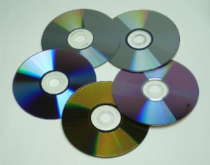 Abbildung 2: Alle fünf beschreibbaren DVD-Medien im Überblick: links oben DVD-RW, rechts oben DVD+RW, links unten DVD-R, rechts unten DVD+R und unten DVD-RAM. Deutlich sind die unterschiedlichen Reflekionseigenschaften zu erkennen